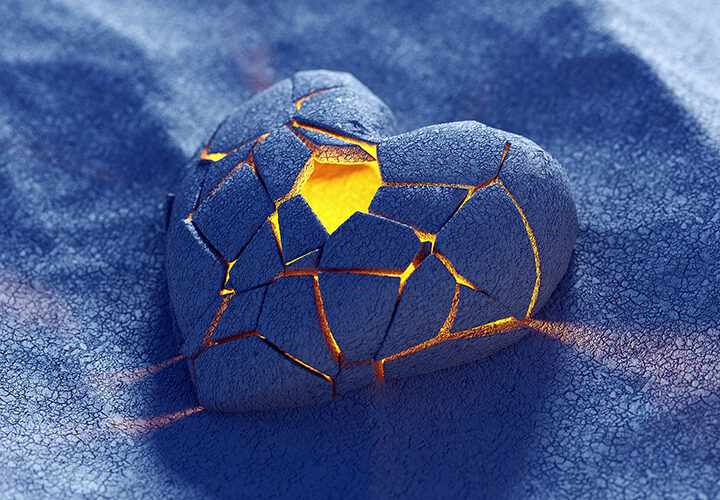 Corazón de arena azul cuarteado, con luz amarilla interior, sobre arena idéntica a con la que está hecho