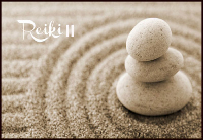 Piedras en equilibrio con círculos concéntricos sobre arena de playa y con el título Reiki II.